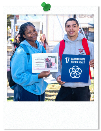 Photo of two students at an SDG mural unveiling event, holding posters representing the 17th sustainable development goal.
