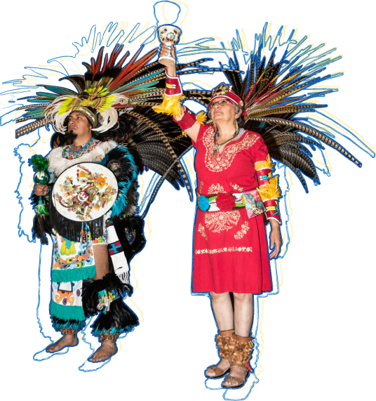 Photo of performers from the World Heritage City Celebration. Two dancers stand next to each other in their cultural costumes, which are colorful with headresses full of feathers. One performer holds a chalice high in the air.