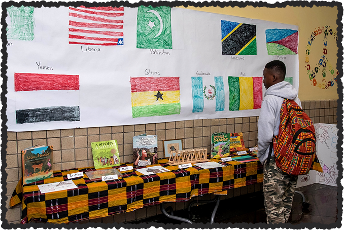 Photo of student in front of poster of flags and other artwork.